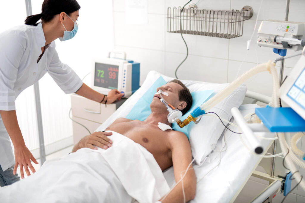 Nurse adjusting medical equipment while patient lies in hospital bed under ventilator treatment