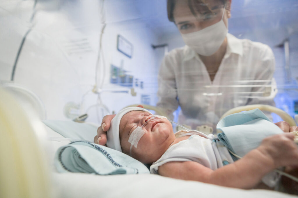 Loving mother looking at her newborn child in an incubator with a face mask during ventilator treatment